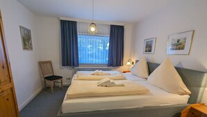 A bedroom with a bed, a chair, a radiator, and a window with curtains. - Am Museum - Holiday cottage Am Museum (Wyk auf Föhr)