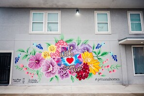 Ein Gebäude mit einem farbenfrohen Wandbild, das Blumen zeigt und den Text „With Corpus Christi“ enthält.