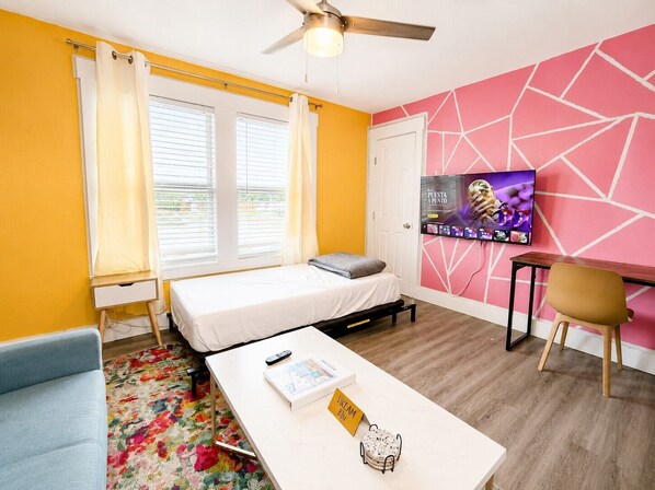 A room with a bed, a desk, a chair, a TV, and a ceiling fan.