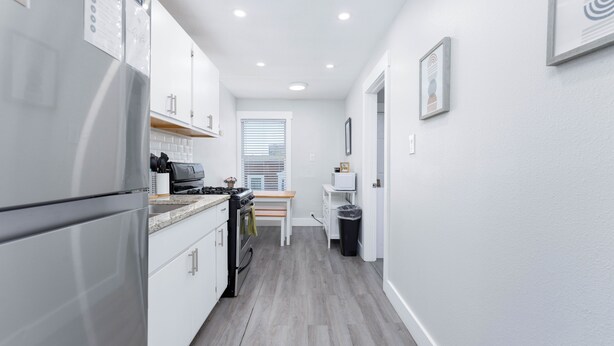 A narrow kitchen with white cabinets, a refrigerator, a stove, and a window with blinds. - 2BDR+Extd Stay Discounts+Central+RemoteWork (Corpus Christi)
