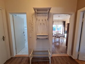 A hallway with a wooden bench, a wall-mounted shelf, and a door leading to a dining area. - Austernfischer - Holiday apartment Austernfischer, own beach chair in the 1st row (Wyk auf Föhr)