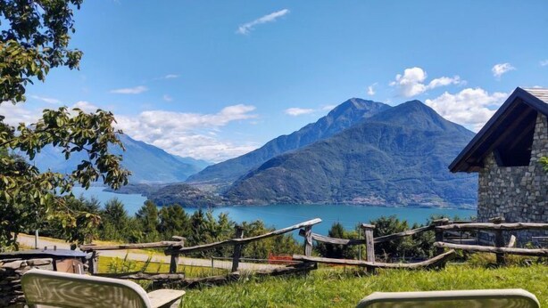 Vista de un lago de montaña con un edificio de piedra y dos sillas de metal en primer plano.