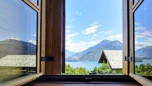 Vista desde el interior de una habitación con ventanales amplios, con vistas a un lago y montañas.