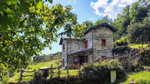 Una casa de piedra con techo inclinado, valla de madera y un muro de piedra.