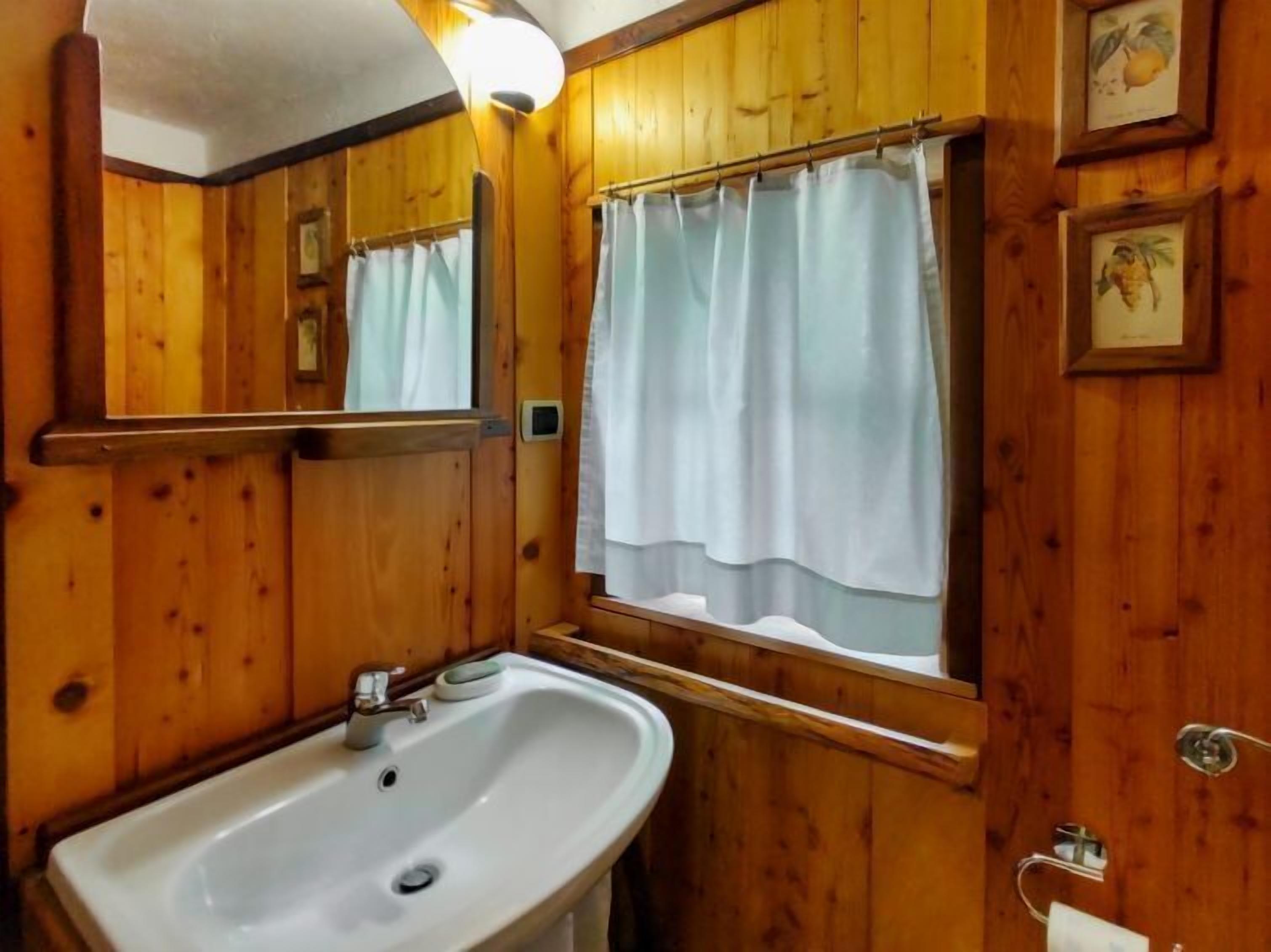 A wooden bathroom with a sink, mirror, and window with a curtain.