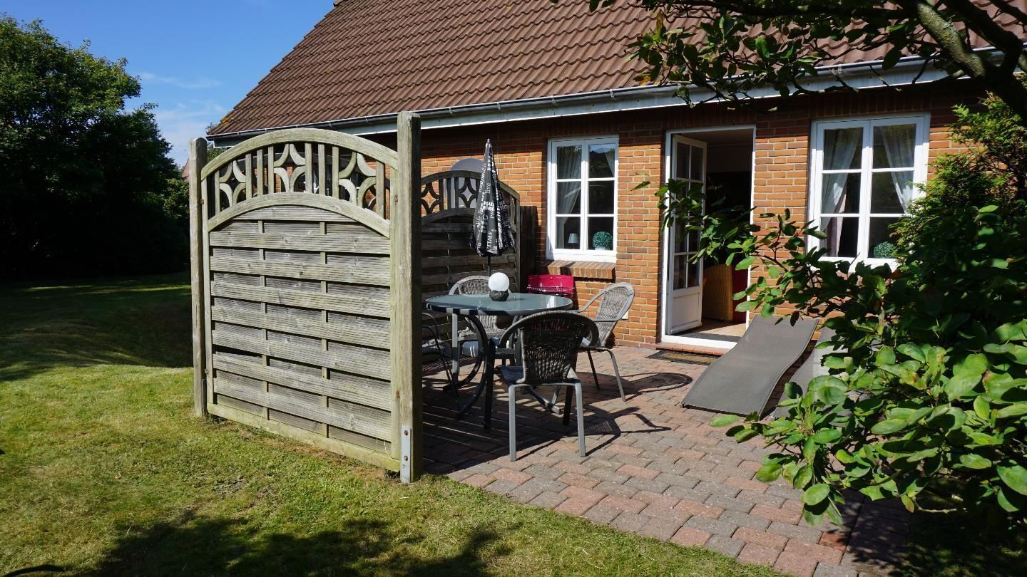 Ein Haus mit Ziegelaußenwand, einem hölzernen Tor, einer Terrasse mit Tisch und Stühlen und einem kleinen Garten.