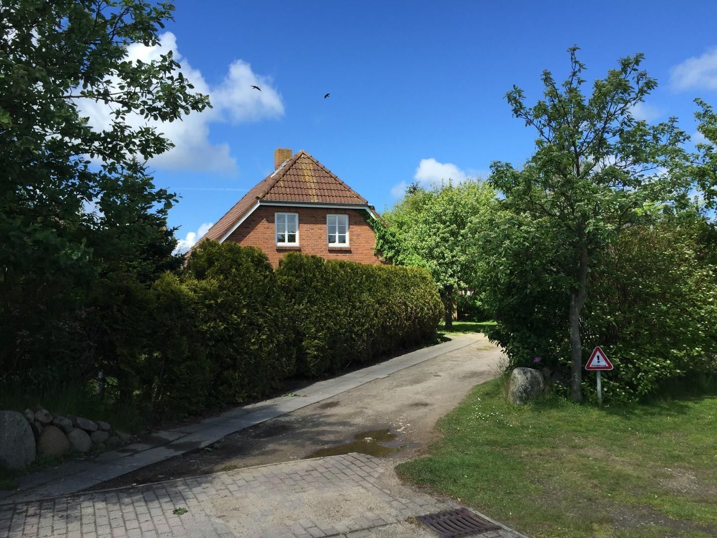 A brick house with a tiled roof, a paved driveway, and a triangular warning sign.