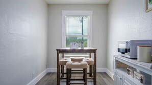 A room with a wooden table and two upholstered chairs, a window with blinds, and a kitchenette area with a microwave and a coffee maker. - Central 1BDR+RemoteWork+Extended Stay+Pets OK (Corpus Christi)