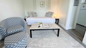 A small, modern bedroom with a bed, a bedside table, and a nightstand. There is a white wall with decorative window panes and a small framed picture. - Central 1BDR+RemoteWork+Extended Stay+Pets OK (Corpus Christi)