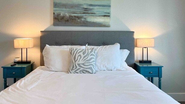 A neatly made bed with white linens and two pillows, flanked by two nightstands with lamps, in a room with a simple, clean design. - Central 1BDR+RemoteWork+Extended Stay+Pets OK (Corpus Christi)