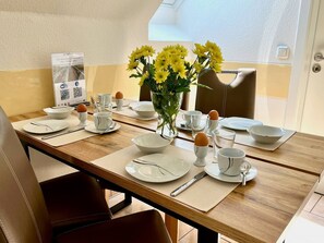 A dining table set with white plates, cups, and cutlery, a vase with yellow flowers, and a QR code on a brochure.