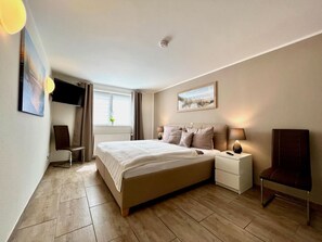 Ett modernt hotellrum med en stor säng, sängbord, en stol, en TV och ett fönster med gardiner.