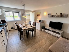 A modern kitchen with a dining area, a TV, and a shelf with decorative items.