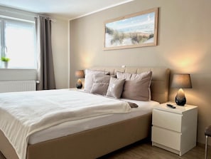 A neatly arranged bedroom with a bed, bedside tables, and a painting on the wall.