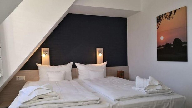 A modern hotel room with a large bed, two bedside tables, a dark accent wall, and a sunset painting. - Comfortable non-smoking apartment Die Remise Marengo RE-11 on Usedom - The (Stolpe auf Usedom)