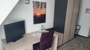 A room with a desk, a chair, a television, a wardrobe, and a poster of a sunset. - Cozy vacation apartment Remise Bayard RE-12 in idyllic village on Usedom - (Stolpe auf Usedom)