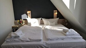 A bedroom with two beds, a dark headboard, and a small bedside table with a lamp and books. - Cozy vacation apartment Remise Bayard RE-12 in idyllic village on Usedom - (Stolpe auf Usedom)