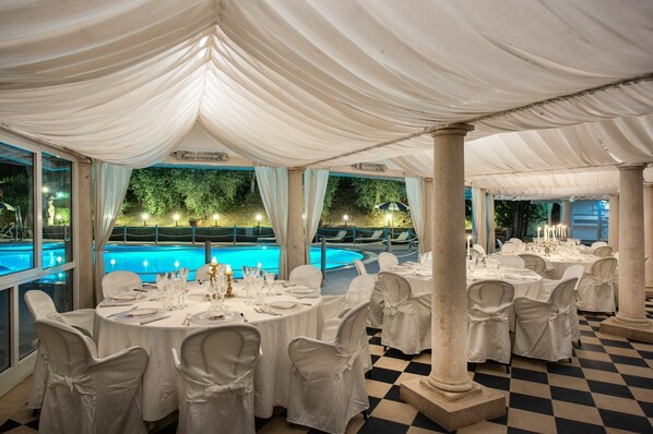 A banquet hall with round tables set for dining, a pool area visible through large windows, and a checkered floor pattern. - Beautiful private villa for 14 people with A/C, private pool, WIFI (Montecatini Terme)