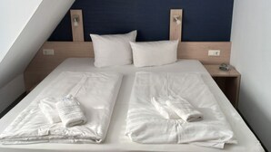 Un lit double avec du linge de lit et des serviettes blanches, une tête de lit en bois et une table de chevet avec une horloge numérique.