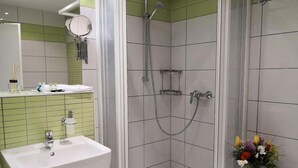 Une salle de bain avec une douche, un lavabo et un petit tabouret sur lequel est posé un vase de fleurs.