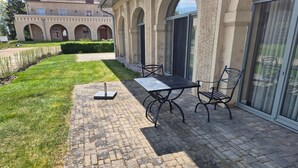 Ein Patio mit Tisch und Stühlen, ein Pflasterweg und ein Gebäude mit Rundbogenfenstern und einer Tür.