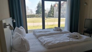 Ein Hotelzimmer mit zwei Betten, einem Fernseher und Blick auf einen Park und ein Gebäude.