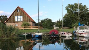 Ein Holzhaus mit rotem Dach, ein Steg mit mehreren Booten und ein ruhiges Gewässer, das die Umgebung spiegelt.