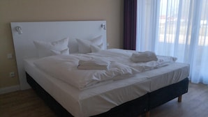 Un lit bien fait, avec du linge de lit blanc et des oreillers, dans une pièce au plancher en bois et aux murs unis.