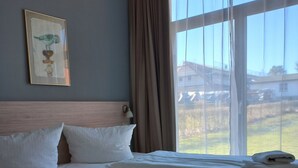 Ein Hotelzimmer mit zwei Betten, einem Kopfteil, einem gerahmten Bild an der Wand und Blick nach draußen.