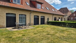 Ein zweistöckiges Haus mit Ziegeldach, einer überdachten Terrasse mit Tisch und Stühlen sowie einem gepflegten Rasen.