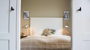 A bedroom with a white headboard, two bedside tables with lamps, a bed with a plaid blanket, and two wall-mounted picture frames. - Die Remise Lexington RE-03 Holiday apartment with terrace on Usedom - Die Remise (Stolpe auf Usedom)