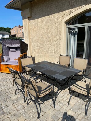 An outdoor patio with a table and chairs, a covered seating area, and a sliding glass door. - The Remise Halla RE-04 - rural luxury holiday apartment with terrace on Usedom - (Stolpe auf Usedom)