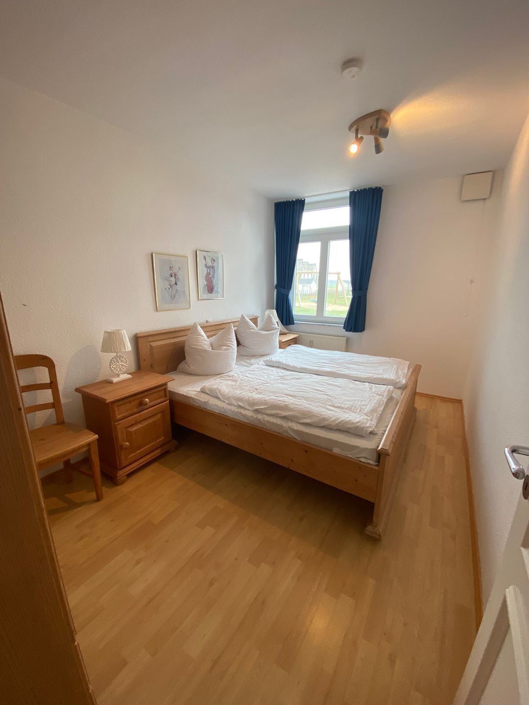 Une chambre à coucher avec un lit en bois, une table de chevet, une chaise et une fenêtre avec des rideaux.