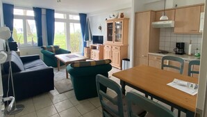 A spacious living area with a sofa, a dining table with chairs, and a kitchen area with cabinets and a coffee machine.