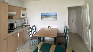 A compact kitchen with a dining table and chairs, a microwave, and a painting on the wall.