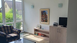 A modern living room with a sofa, a coffee table, a wicker chair, a TV, and a bookshelf.