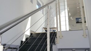 Un escalier doté d’une main courante en métal et d’une balustrade en verre, menant à un palier avec une porte.