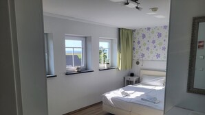 Une chambre à coucher avec un lit, deux fenêtres, une table de chevet, un miroir et un plancher en bois.
