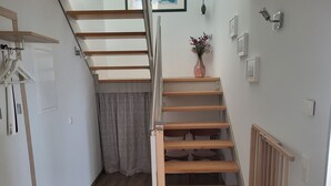 Un couloir étroit avec un escalier en bois, un radiateur et une petite table sur laquelle est posé un vase de fleurs.