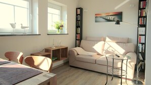 Un salon avec un canapé, une table basse en verre, une bibliothèque et un tableau accroché au mur.