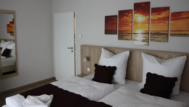 A hotel room with two beds, a wooden headboard, white bedding, and a wall with sunset paintings. - Cozy vacation apartment Landhof Schwalbennest LH-204 quiet village location on Usedom (Stolpe auf Usedom)