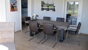 Un comedor con mesa de madera y seis sillas, lámpara colgante y obras de arte en las paredes.
