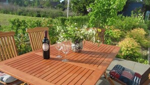 Mesa de madera al aire libre con una botella y vasos, rodeada de sillas con cojines estampados.