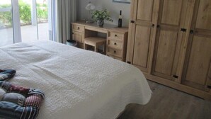 Un dormitorio con una cama grande, un escritorio de madera, un armario y vistas a la vegetación exterior.