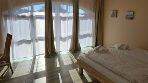 A bedroom with a bed, a chair, and a large window with curtains. - Cozy vacation apartment Landhof Weide LH-202 in a quiet village idyll on Usedom - (Stolpe auf Usedom)