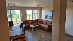 A living room with a sofa, coffee table, and dining table. - Cozy vacation apartment Landhof Weide LH-202 in a quiet village idyll on Usedom - (Stolpe auf Usedom)