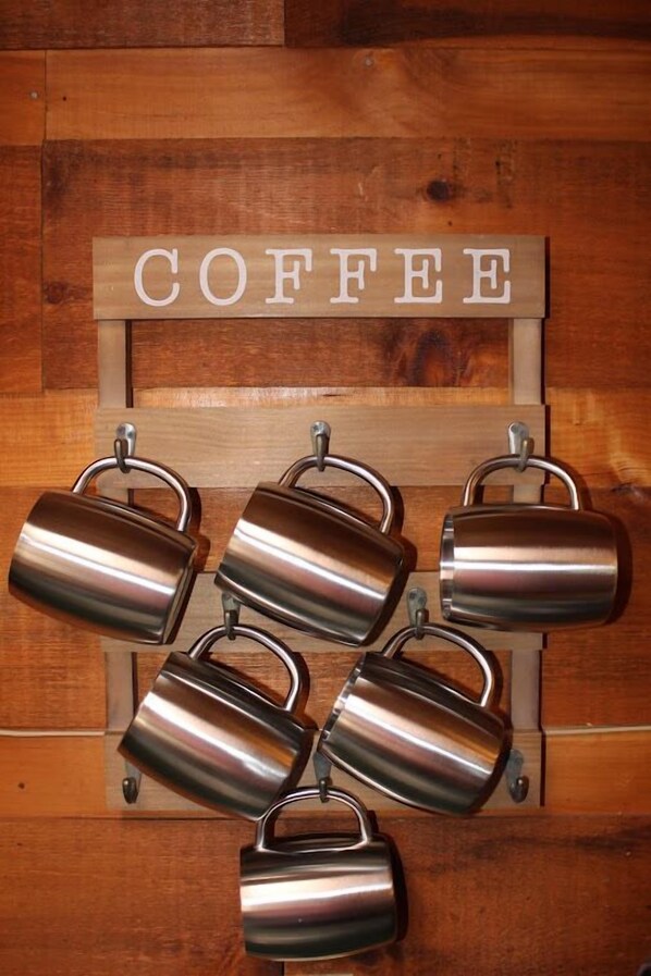 A wooden sign with the word "COFFEE" hanging above a set of six stainless steel mugs.