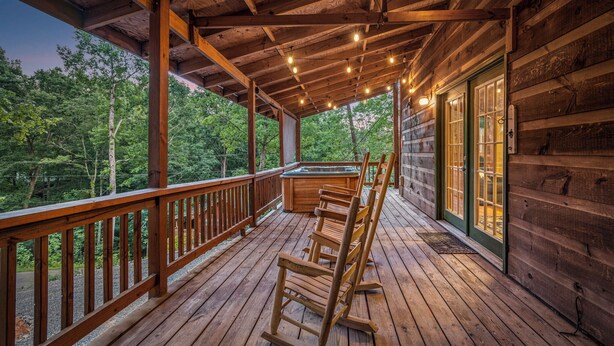 A wooden deck with a hot tub, rocking chairs, and a covered area with string lights. - 2 King Beds - Hot Tub - 10 min to parkway (Sevierville)