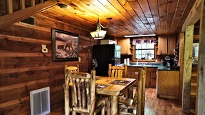 A rustic wooden interior with a dining table and chairs, a refrigerator, and a kitchen area. - 2 King Beds - Hot Tub - 10 min to parkway (Sevierville)