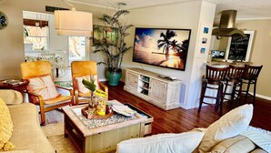 Una sala de estar con un sofá, sillones, una mesa de centro, un televisor, una zona de comedor con sillas y una planta grande en maceta.